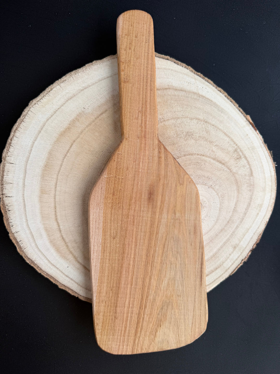 Light wood spanking paddle on a wood slice against a dark background — impact play guide by Spanked It!