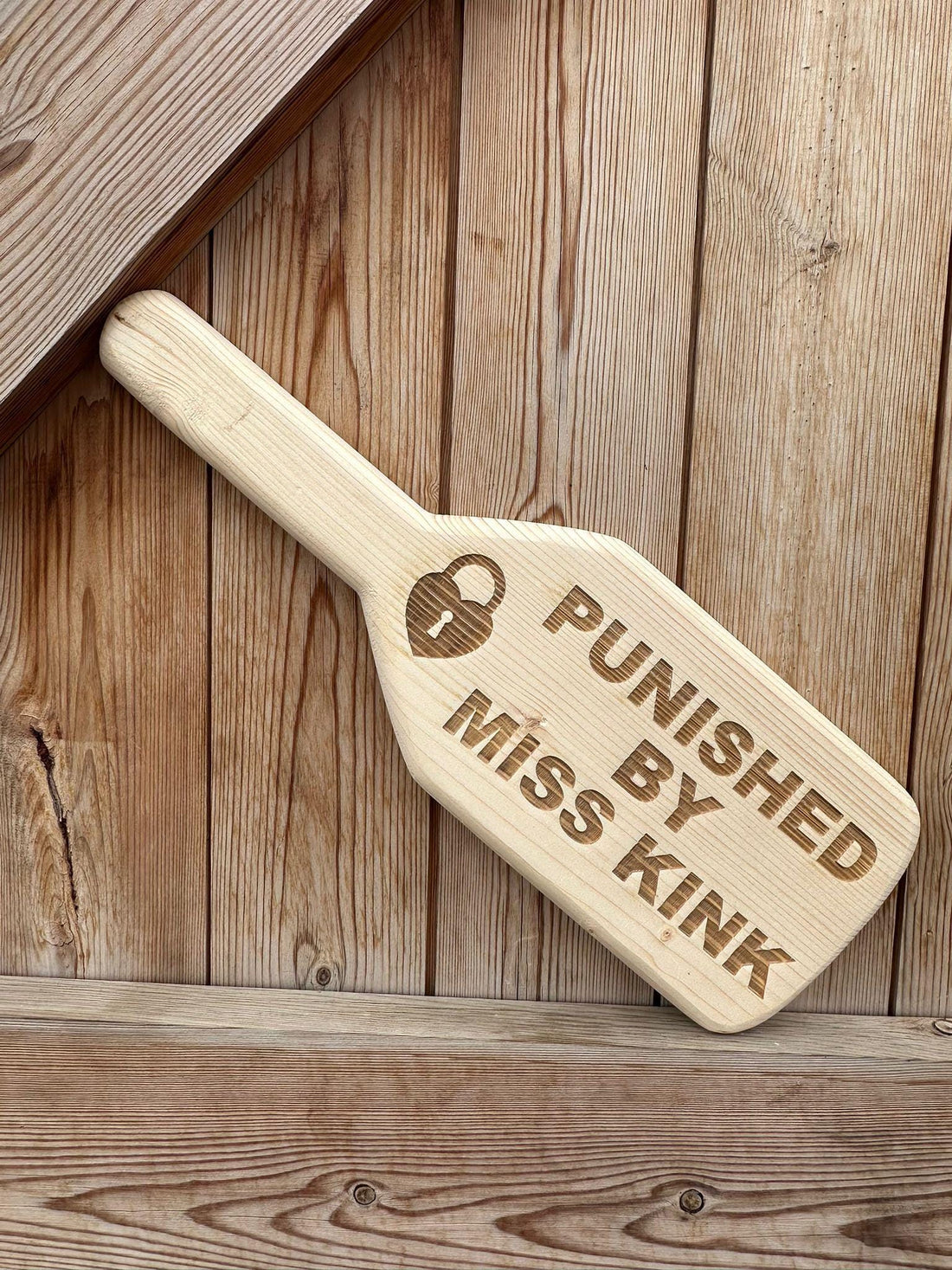 Personalised engraved spanking paddle on rustic wood background — luxury BDSM gift for couples handcrafted in the UK